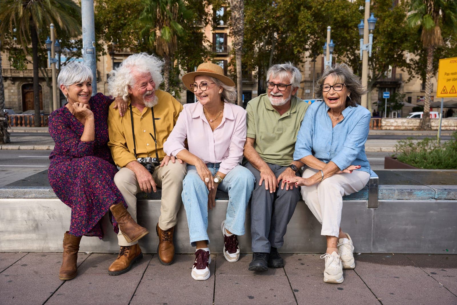 Cinco adultos mayores sonrientes sentados juntos en un banco de la ciudad