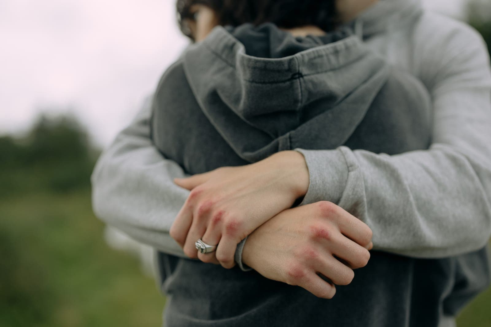 Esposa abrazando a su esposo por la espalda; se ven sus manos con los anillos de matrimonio